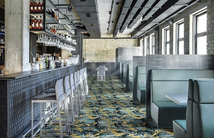 Stylish restaurant in a loft style with brick walls and a concrete column. There is a textured bar rack with chairs, shelves with bottles and glasses, bar equipment, sofas with tables and partitions.